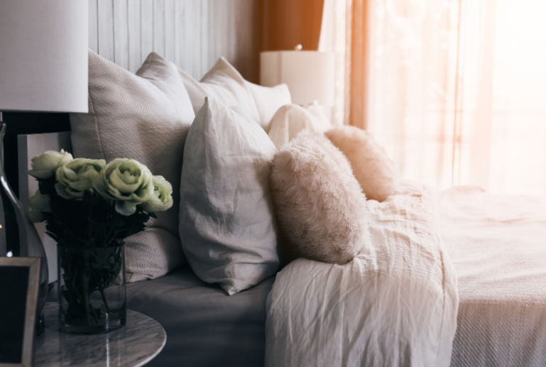 cozy made bed with fuzzy pillow and a night stand with  fresh flowers