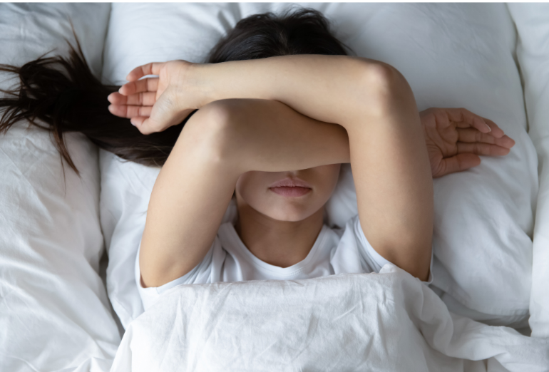 girl laying in bed with arms crossed over her face, tired