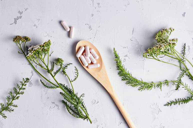 medicine capsules on a wooden spoon, surrounded by 3 springs of greenery